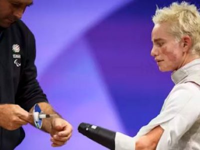 A female para athlete watches as her coach approaches with a prosthesis for her fencing competition. 